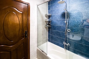 Una puerta de madera y una zona de ducha con paredes de azulejos azules y cerramiento de vidrio.