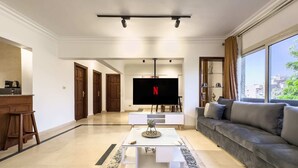 A modern living room with a flat-screen TV, a sofa, a coffee table, and a kitchen area with a bar stool. - Xuru Stays I The 2bdr Velvet Vibe @ Maadi (Cairo)