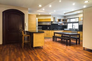 A modern kitchen with wooden flooring, a dark wooden door, and a dining area with a bench. - Xuru Stays I The Luxe Loft 2bdr Apt. @ Maadi (Cairo)