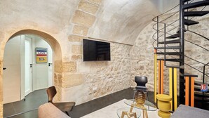 Un interior moderno con una pared de piedra, una escalera espiral negra, un televisor de pantalla plana y un sofá.