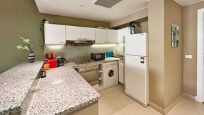 A compact kitchen with white cabinets, a built-in oven, a microwave, and a washing machine. - Xuru Stays I Minimal & Central 1bdr Apt. @ Abu Tig Marina (El Gouna)