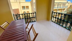 A balcony with a wooden table and chairs, a tiled floor, and a view of buildings with balconies. - Xuru Stays I Minimal & Central 1bdr Apt. @ Abu Tig Marina (El Gouna)