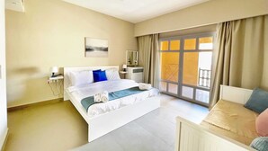 A hotel room with a large bed, a bedside table, a chair, and a window with curtains. - Xuru Stays I Minimal & Central 1bdr Apt. @ Abu Tig Marina (El Gouna)