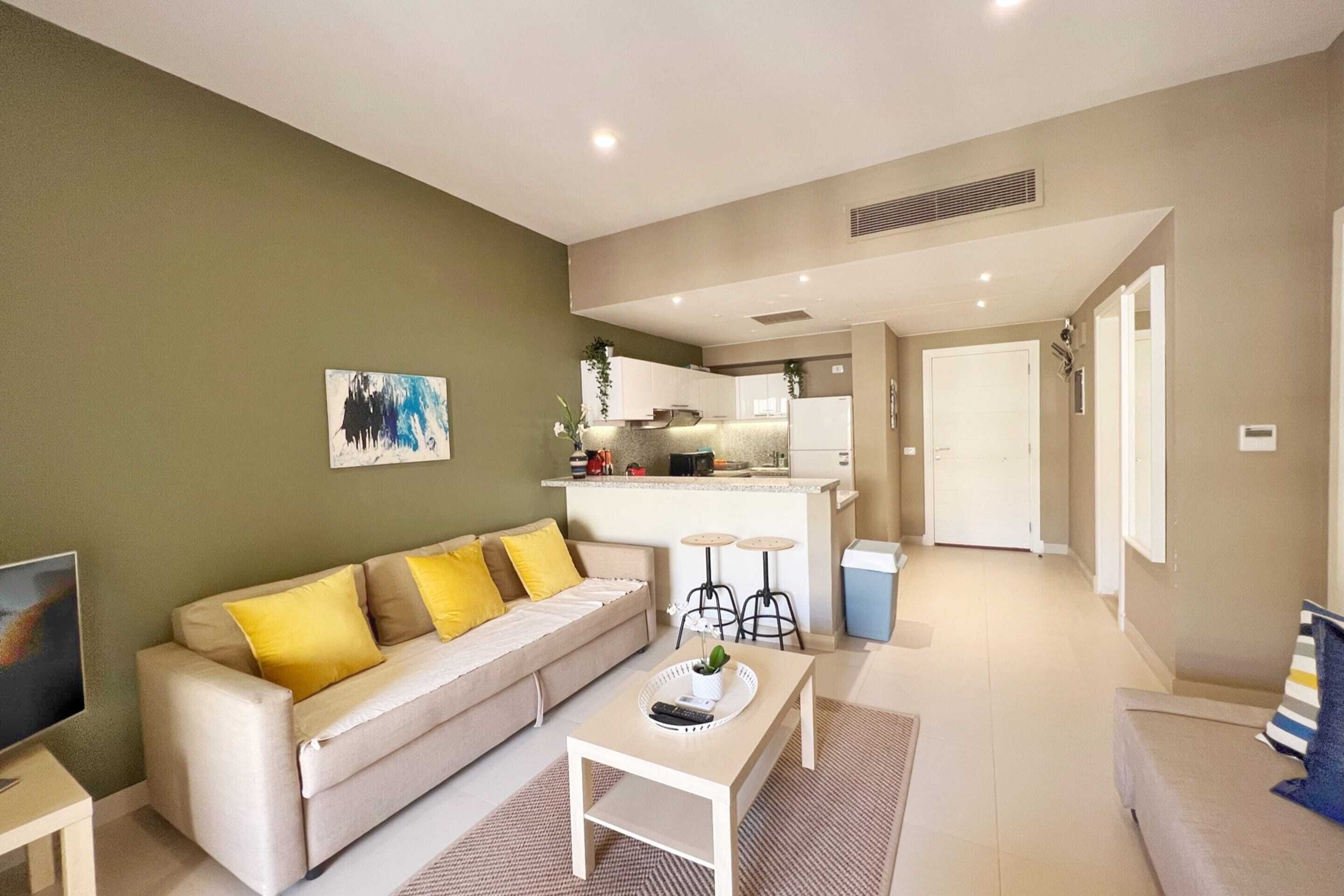 A modern living room with a sofa, coffee table, and a kitchen area in the background.