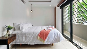 A bedroom with a bed, bedside table, and a window with a view of greenery. - Stylish Studio in Zazil-Ha - Rooftop Pool (Playa del Carmen)