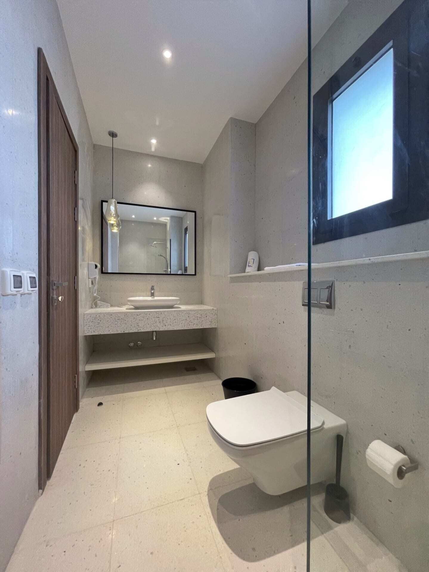 A modern bathroom with a glass partition, a large mirror, a sink, and a toilet.