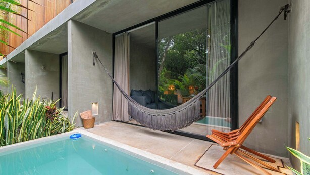 A modern outdoor pool area with a hammock, wooden chair, and a view of greenery through a glass door. - Seremonia Origen - Tulum Studio with Plunge Pool (Tulum)