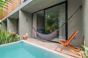 A modern outdoor pool area with a hammock, wooden chair, and a view of greenery through a glass door. - Private Plunge Pool King Studio - Tulum Jungle (Tulum)