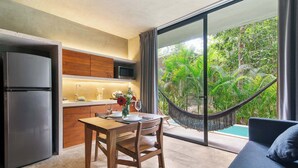 A modern kitchen with a refrigerator, microwave, and wooden cabinets. There is a dining table with chairs and a hammock overlooking a lush garden and pool. - Seremonia Origen - Tulum Studio with Plunge Pool (Tulum)