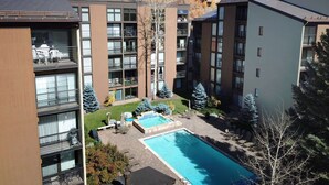 A modern apartment complex with multiple balconies, a swimming pool, and a view of a hilly landscape.