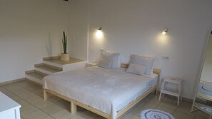 A bedroom with a bed, a nightstand, a small table, a potted plant, and a staircase.