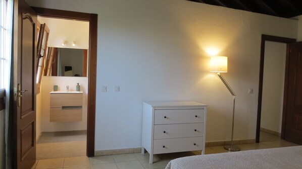 A bedroom with a white dresser, a bedside lamp, and a mirror above the dresser.