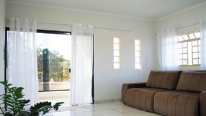 A living room with a brown sofa, large windows with white curtains, and a view of the outdoors.