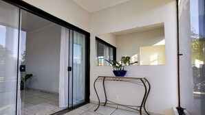 A modern apartment with a sliding glass door leading to a balcony, a small table with a potted plant, and a large mirror on the wall.
