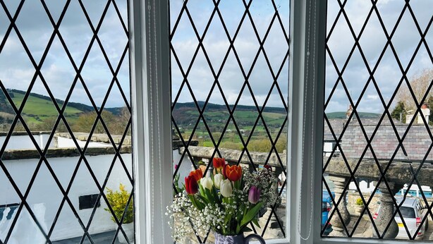 A window with a view of a river and hills, a purple vase with flowers, and a stone balustrade. - Pentre Cerrig Country House (Mold)