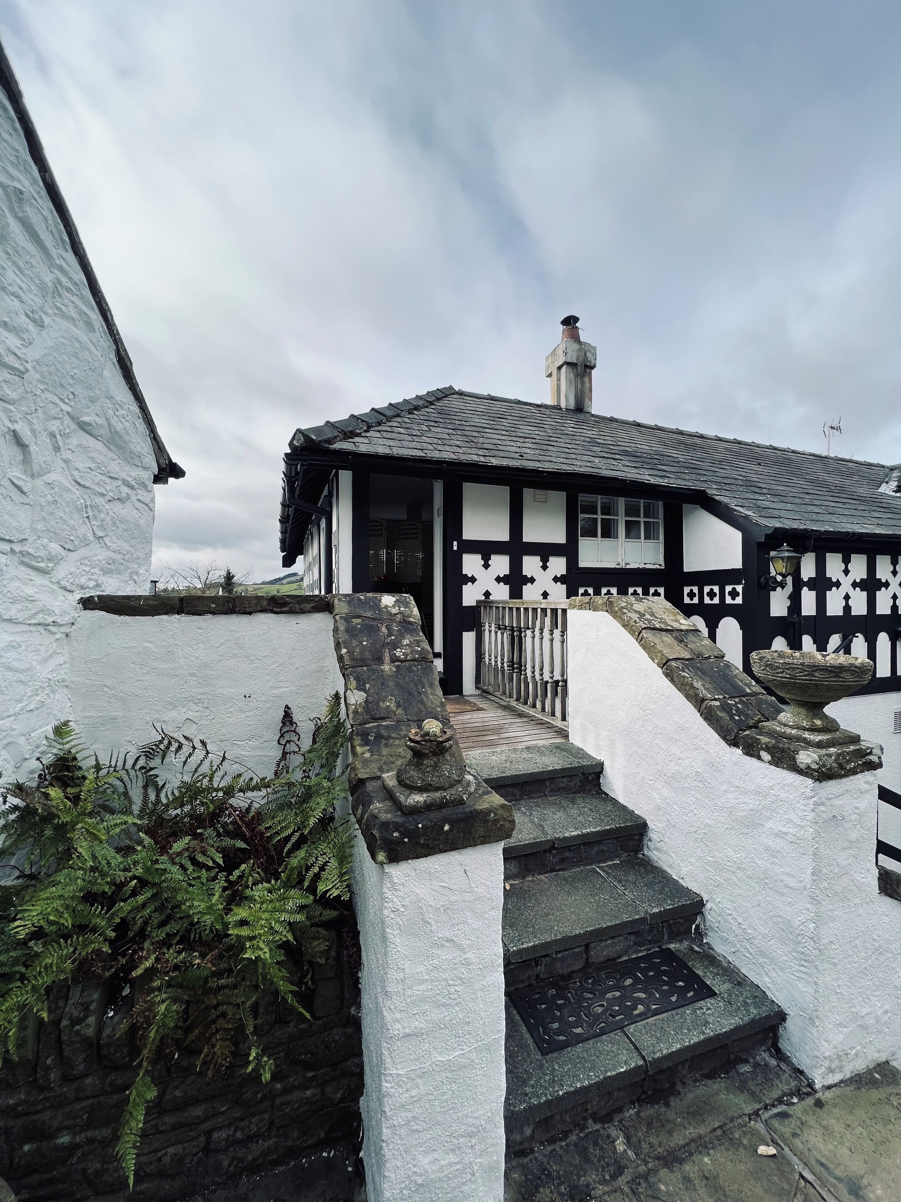 A traditional black and white half-timbered house with a stone staircase leading to the entrance.