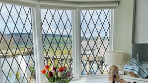 A dining area with a table set for two, a chair, and a view through a window with a metal grid. - Pentre Cerrig Country House (Mold)