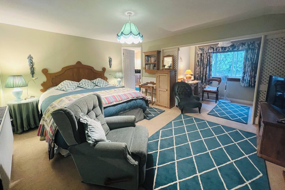 A bedroom with a bed, a chair, a desk, a wardrobe, and a view of the outside.