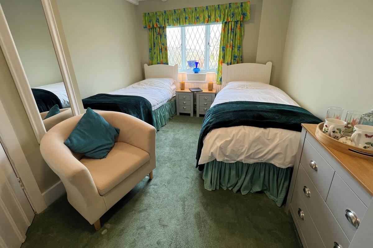 A bedroom with two beds, a chair, a dresser, and a window with curtains.
