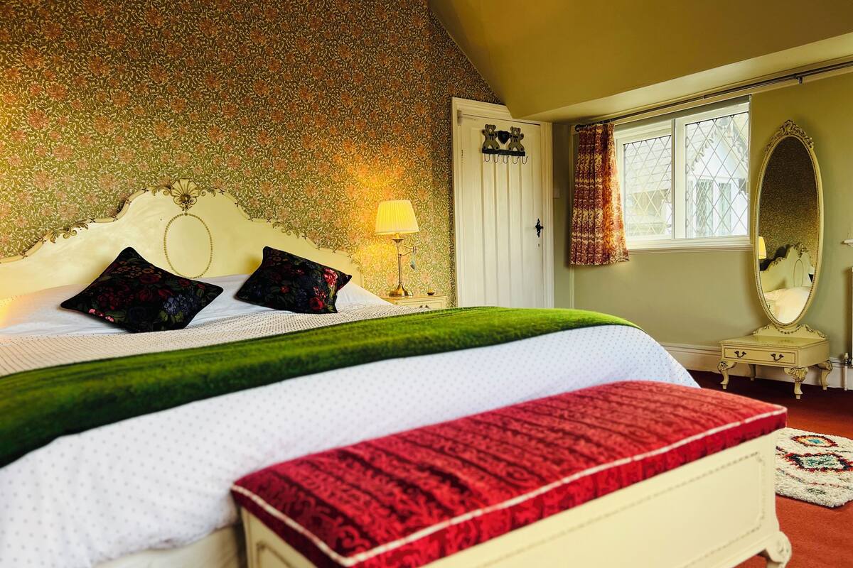 A bedroom with a large bed, a nightstand, a mirror, and a window with curtains.