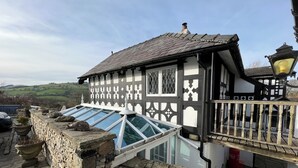 A traditional black and white half-timbered house with a sloped roof, a stone wall, and a glass conservatory. - Pentre Cerrig Country House (Mold)