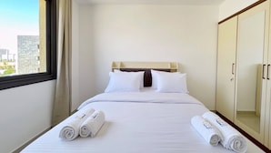 A hotel room with a bed, two rolled towels, a wardrobe, and a window with curtains. - Refreshed & Uplifted 2 BDR @ G Cribs (El Gouna)