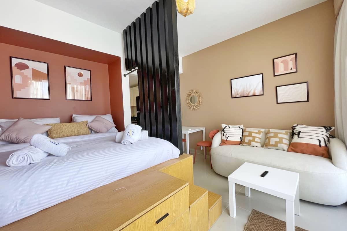 Een moderne hotelkamer met een bed, een bank, een kleine tafel en een bureau. Er hangen ingelijste foto's aan de muren en een spiegel op de muur.