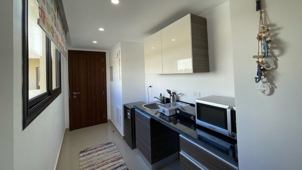 A modern kitchen with a built-in microwave, a sink, and a refrigerator. There is a wooden door and a window on the left side. - Refreshed & Uplifted 2 BDR @ G Cribs (El Gouna)