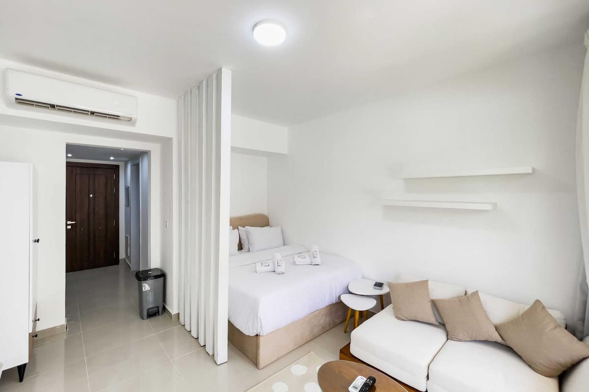 Een moderne hotelkamer met een bed, een witte bank, een klein bijzettafeltje en een prullenbak.