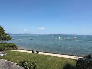 A view of a calm sea with several sailboats and a sandy beach with a few chairs.