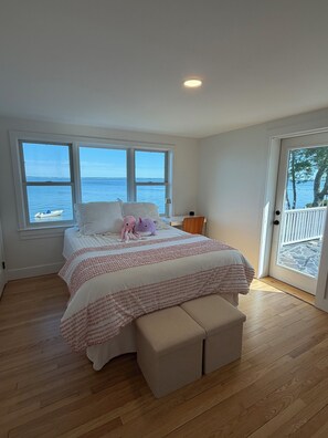 A bedroom with a large bed, a view of the sea through two windows, and a door leading to a balcony.