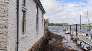 Ein Küstenhaus mit Steinanbau, einer Anlegestelle mit Booten und einer Aussicht auf Wasser und Hügel in der Ferne.