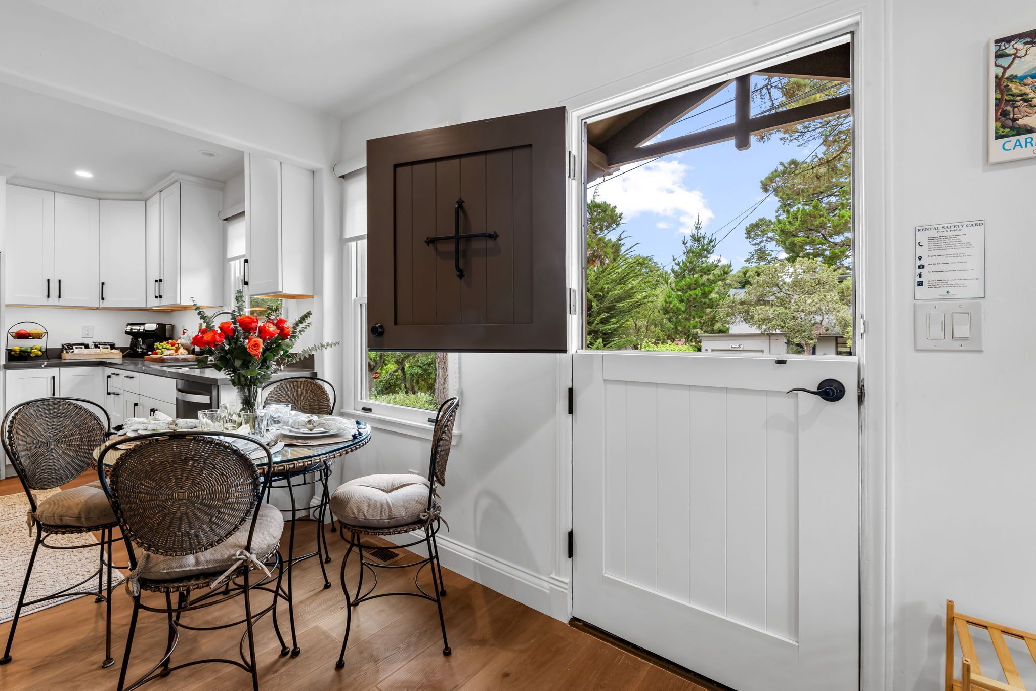 A modern kitchen with white cabinets, a dining table with chairs, and a large window with a view of greenery.