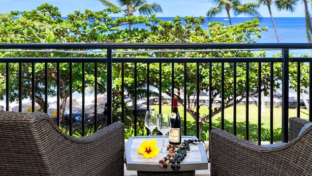 A balcony with wicker furniture, a table with a bottle of wine, glasses, and a lei.