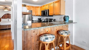 A kitchen with wooden cabinets, a granite countertop, a microwave, and two plaid stools.