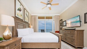 A bedroom with a bed, a ceiling fan, a TV, a dresser, and a balcony with curtains. - Phoenix Orange Beach 603 3 Bedroom Condo (Orange Beach)