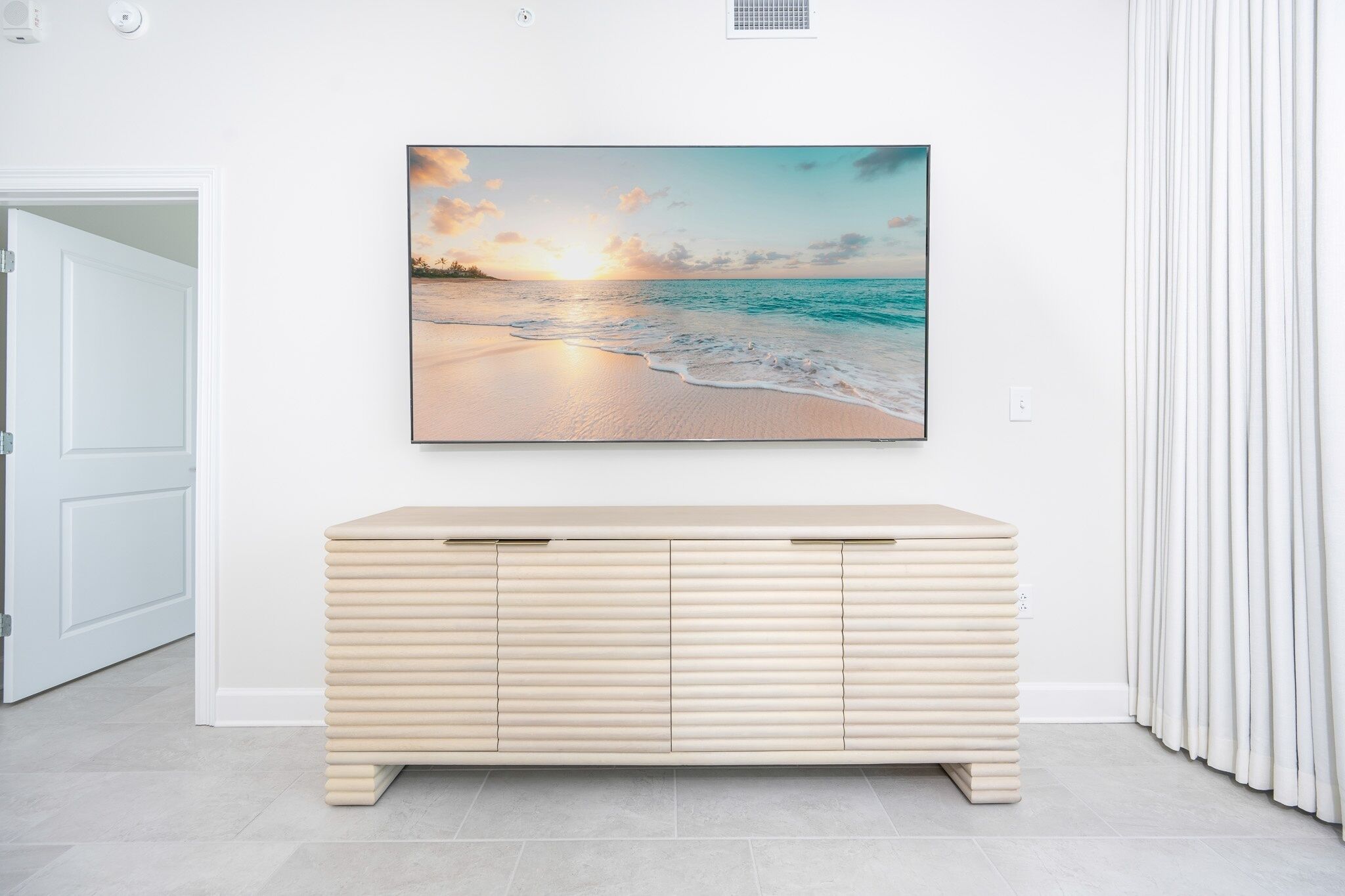 Una stanza con un tavolino consolle color beige, un quadro appeso raffigurante una spiaggia al tramonto e una porta bianca.