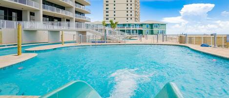 A swimming pool with a slide, surrounded by a wooden deck and a white fence.