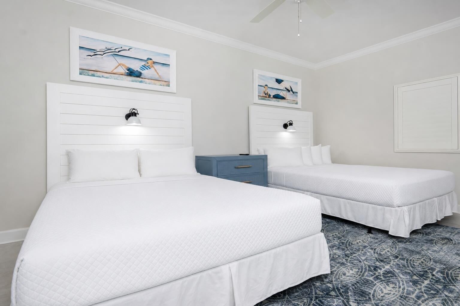 A hotel room with two beds, a blue dresser, and artwork on the walls.