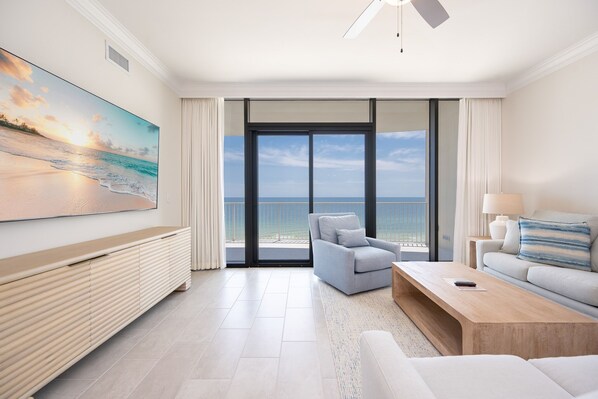 Ein modernes Hotelzimmer mit großem Fenster und Meerblick, einem Wand-Fernseher, einer Couch, einem Couchtisch und einem Deckenventilator.