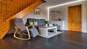 A modern living room with a wooden staircase, grey sofa, and a coffee table with a vase of flowers. - Doppelhaushaelfte in Hasselfelde (Oberharz am Brocken)