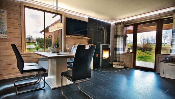 A modern kitchen with a large window, a fireplace, and a dining area with two chairs. - Doppelhaushaelfte in Hasselfelde (Oberharz am Brocken)