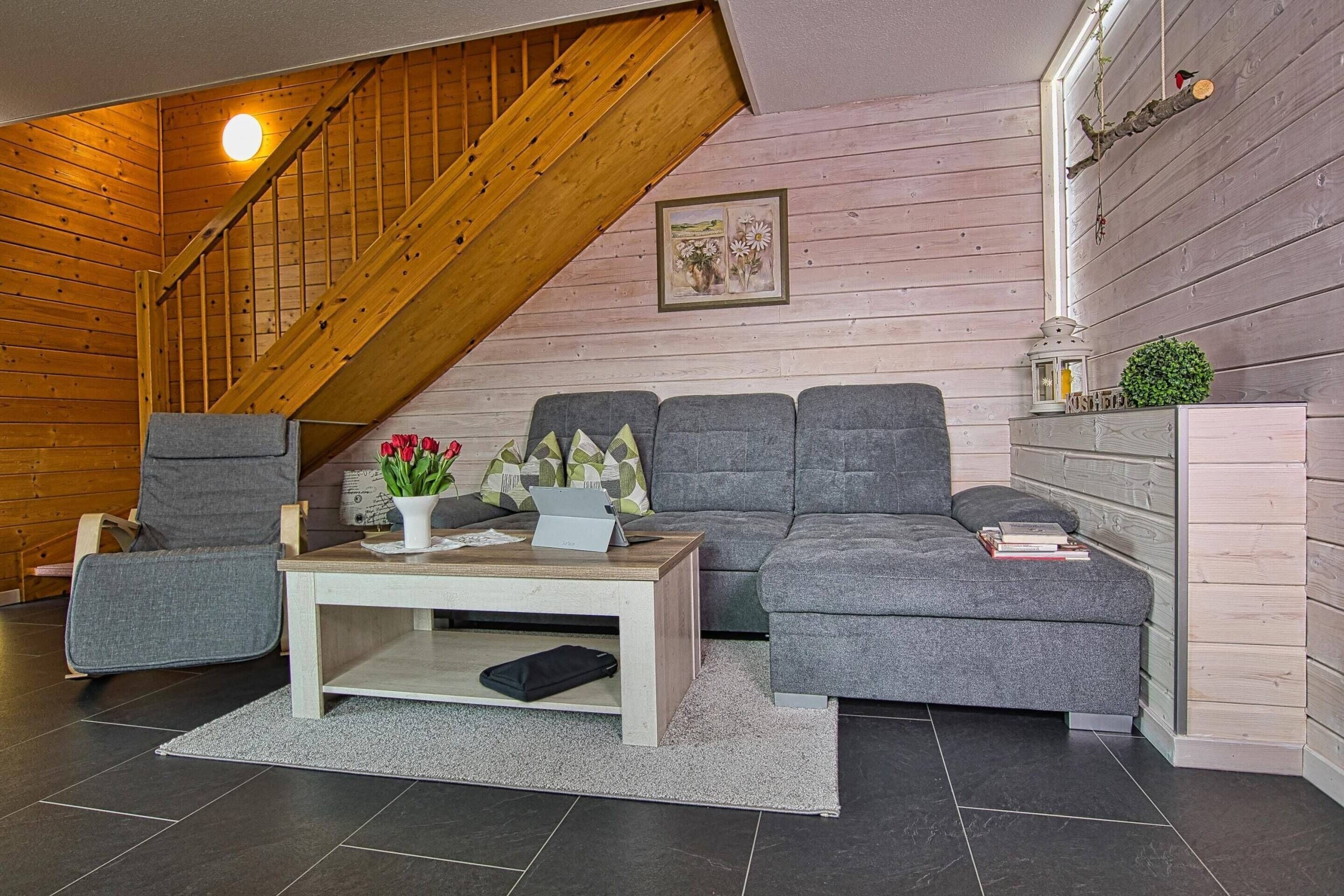 Een gezellige woonkamer met een grijze bank, een houten salontafel en een trap.