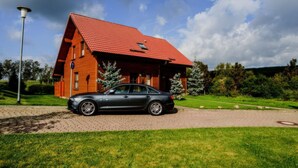 A red-roofed wooden house with a paved driveway and a parked car. - Doppelhaushaelfte in Hasselfelde (Oberharz am Brocken)