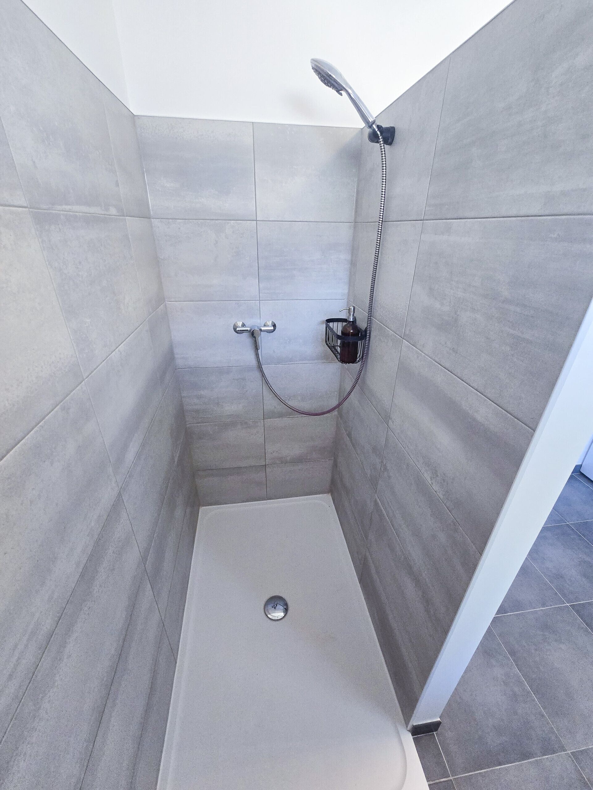 A shower stall with a handheld showerhead and a handheld shower hose.
