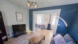 Un salon moderne avec un téléviseur, un canapé, une table basse et un coin repas à l’arrière-plan.