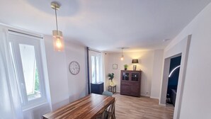 Un vaste espace dédié à la salle à manger, avec une table et des chaises en bois, une horloge au mur et un meuble avec des portes en verre.