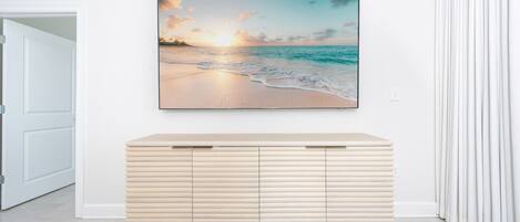 A room with a beige console table, a wall-mounted painting of a beach at sunset, and a white door.
