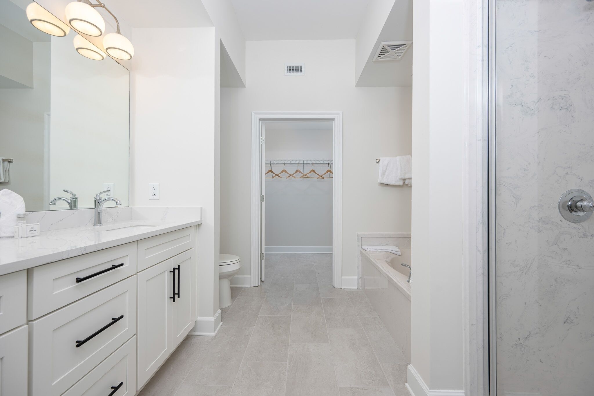 A modern bathroom with a large mirror, white cabinets, a shower enclosure, and a walk-in closet.