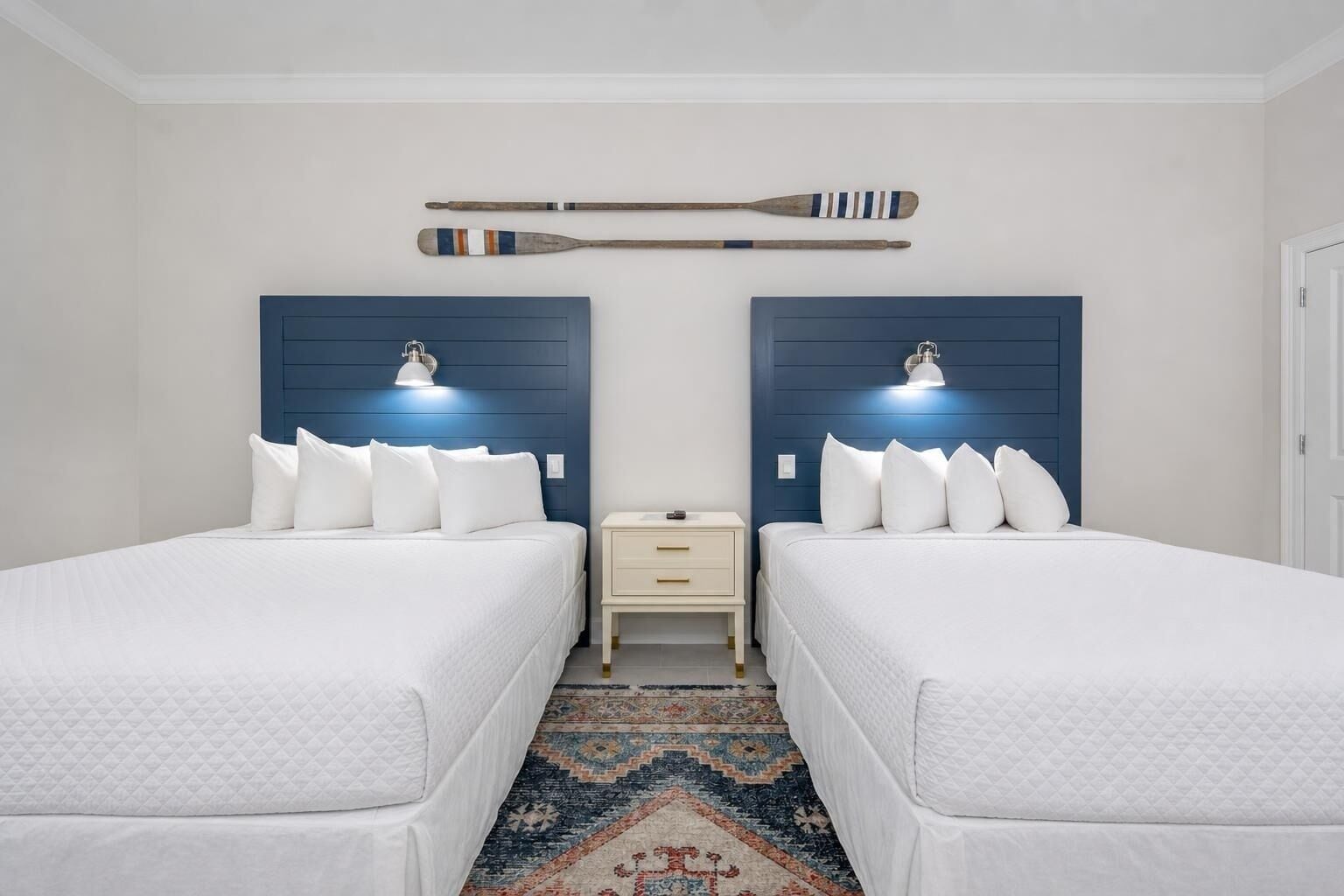 A hotel room with two beds, a nightstand, a wall-mounted lamp, and a decorative wall piece.